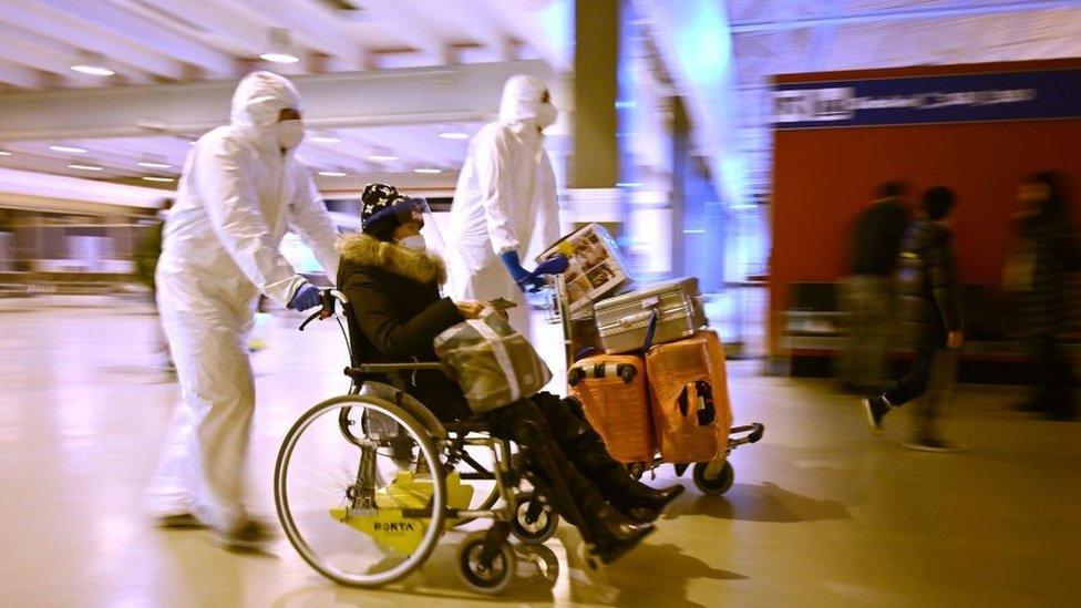 Workers wearing protective masks and suits help a Chinese traveller arriving in Rome