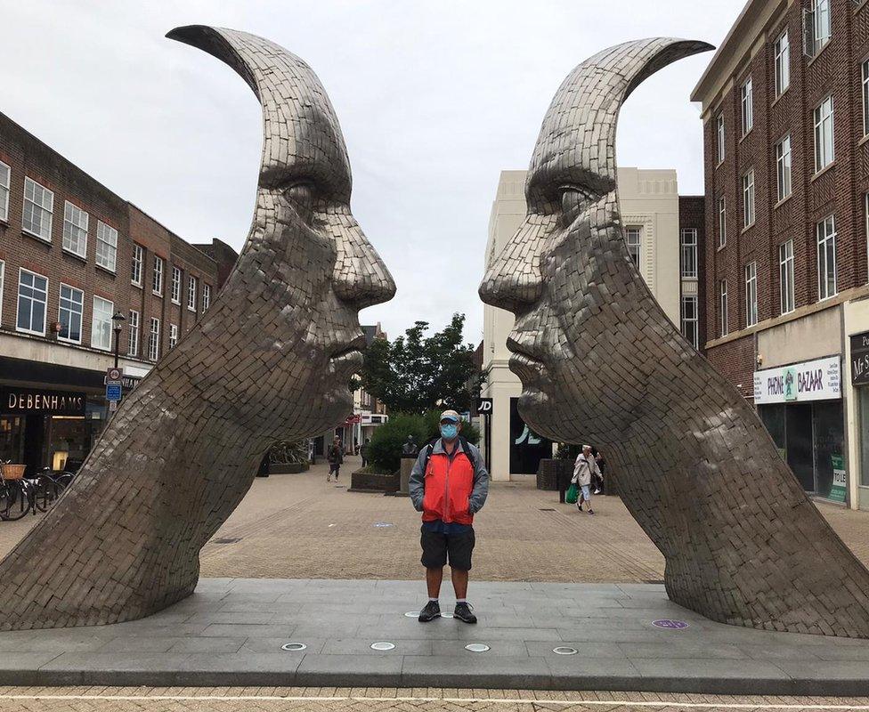 Man wearing a facemask next to Rick Kirby's sculpture in Bedford