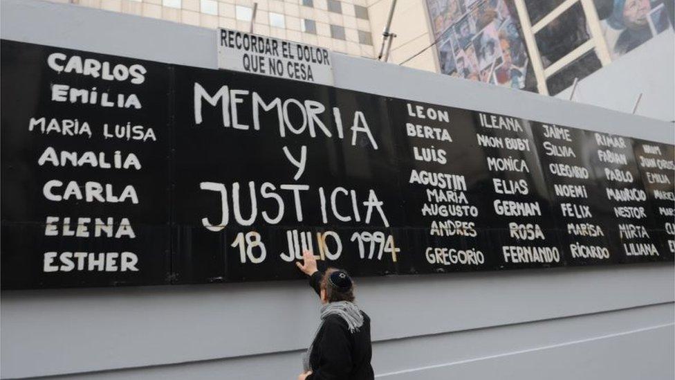 A man touches a billboard with the names of victims during an event to commemorate the 25 years of the attack against the Asociacion Mutual Israelita Argentina (AMIA), in Buenos Aires, Argentina, 18 July 2019