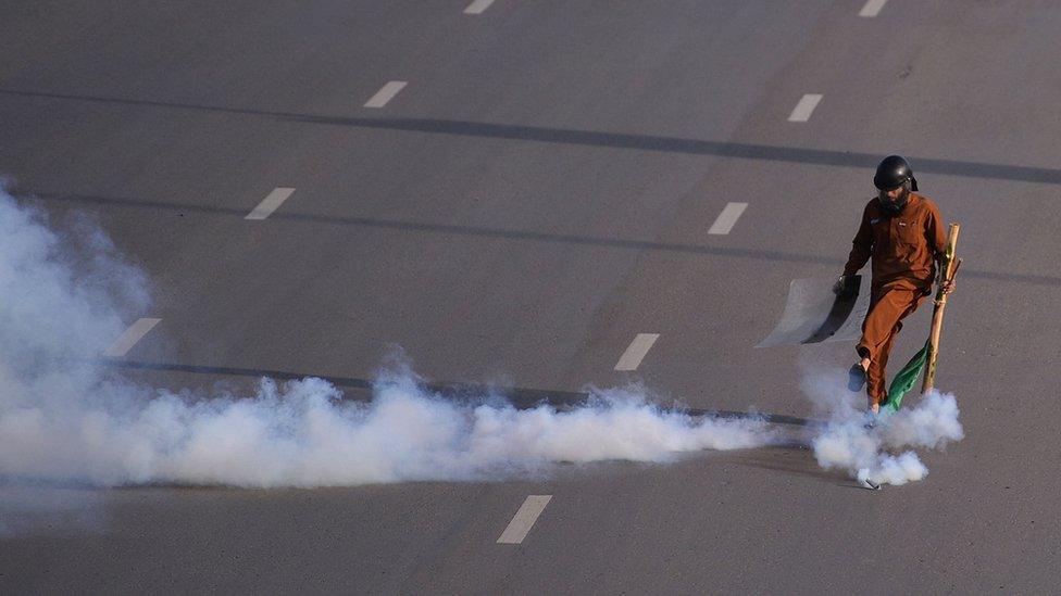 A supporter of executed Islamist Mumtaz Qadri kicks away a tear gas fired by Pakistani anti-riot police officers