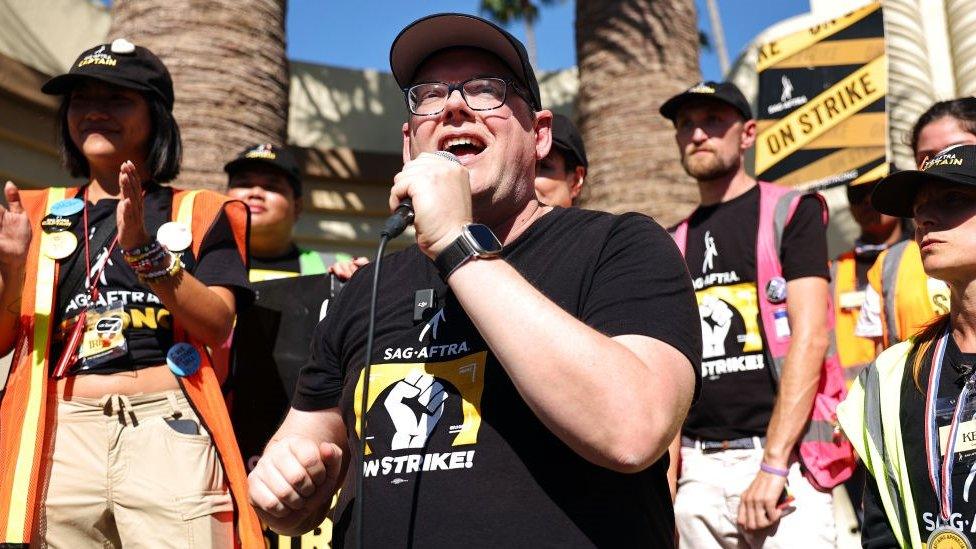 A man holding a microphone on a picket line of strikers