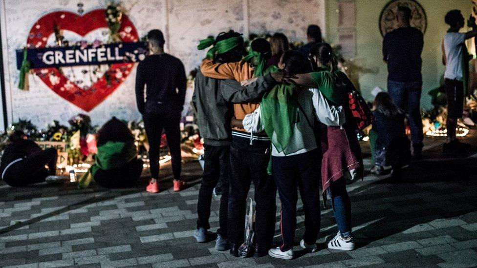 People embrace at the foot of the Grenfell Tower before a memorial