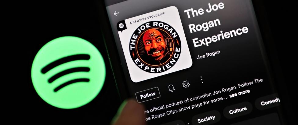 Spotify logo next to an iPhone showing The Joe Rogan Experience