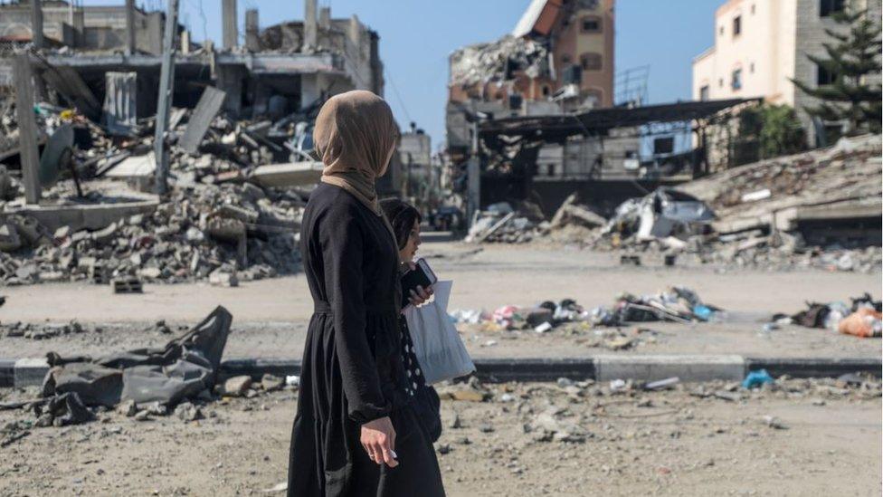 A woman and girl walk past destroyed residential buildings in Al Nuseirat refugee camp