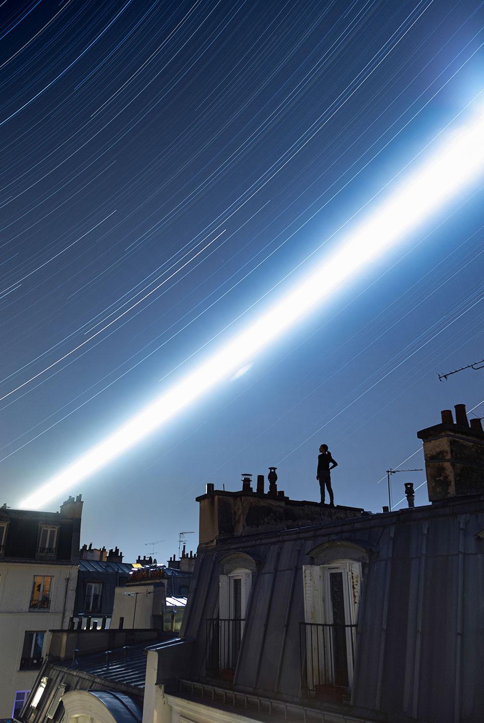 An image showing a woman standing on a Parisian rooftop with a long exposure view of the night sky