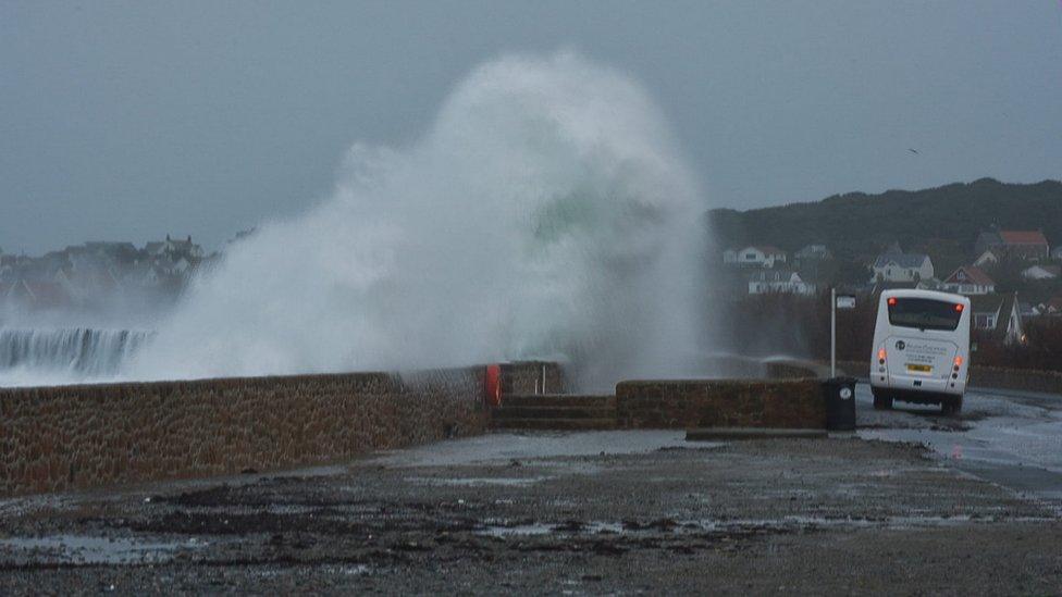 Waves coming over sea wall as bus drives along coast road