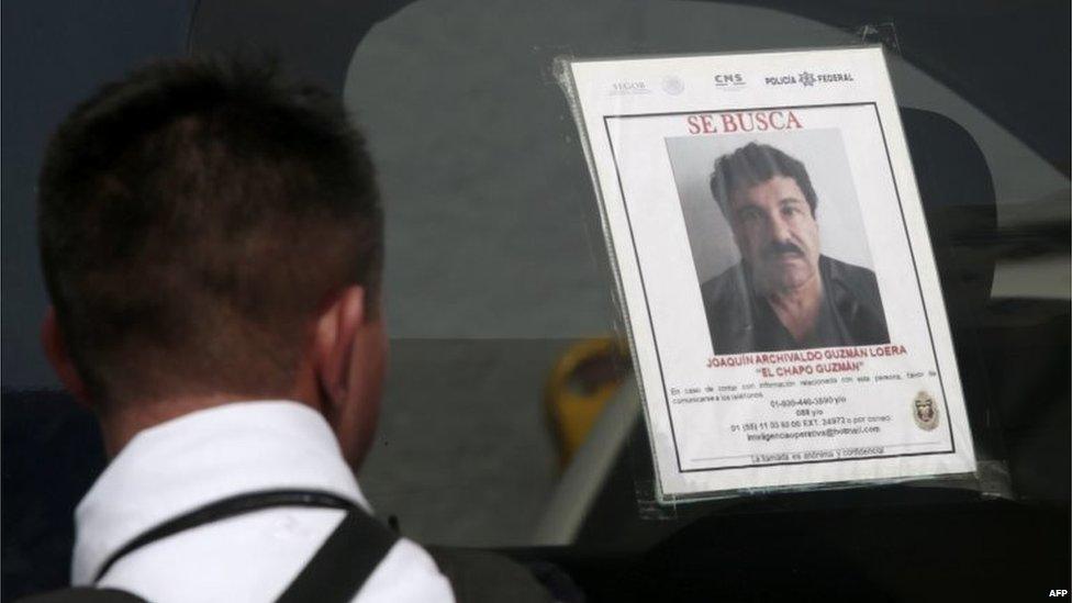 A federal police officer stands next to a patrol car with a picture of fugitive drug lord Joaquin Guzman on 14 July, 2015.