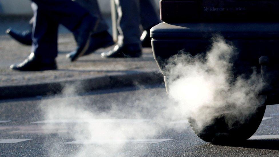 An exhaust pipe of a car on the road while people walk past