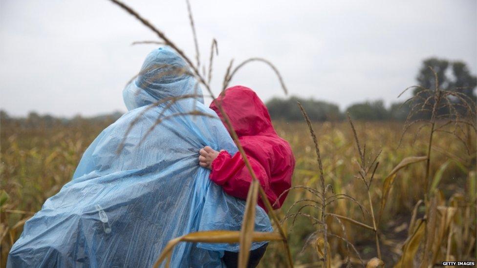 A man holds his child as he walks through corn fields in the rain in an attempt to evade authorities on 10 September 2015 in Roszke, Hungary.