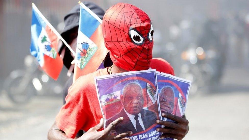 A demonstrator wearing a Spiderman mask holds photos of Supreme Court Judge Joseph Mecene Jean-Louis, as he takes part in a protest against Haiti's President Jovenel Moïse, in Port-au-Prince, Haiti February 14, 2021.