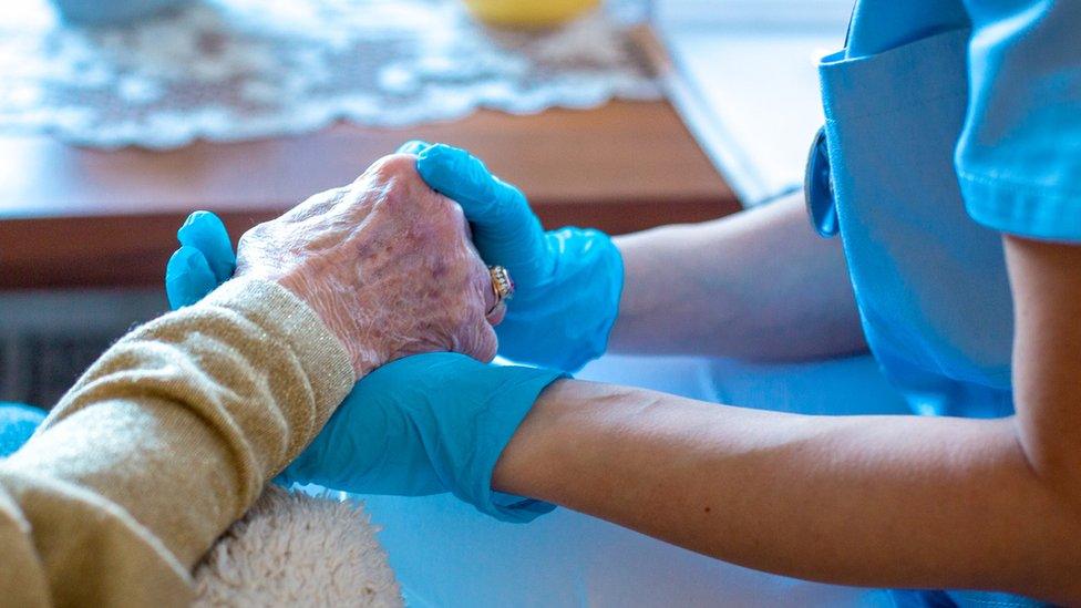 Social worker in PPE holding elderly person's hand