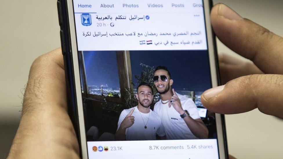 A man holds a mobile phone showing a Facebook post by the Israeli government featuring a photo of Egyptian singer Mohamed Ramadan and Israeli footballer Diaa Saba