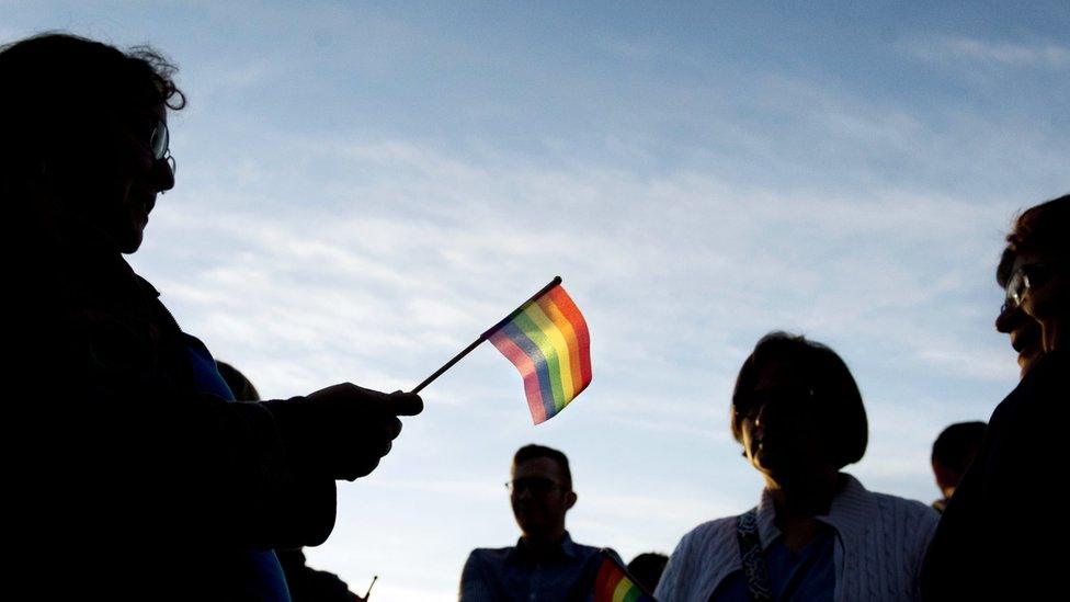 people silhouetted against the sky, holding a rainbow flag