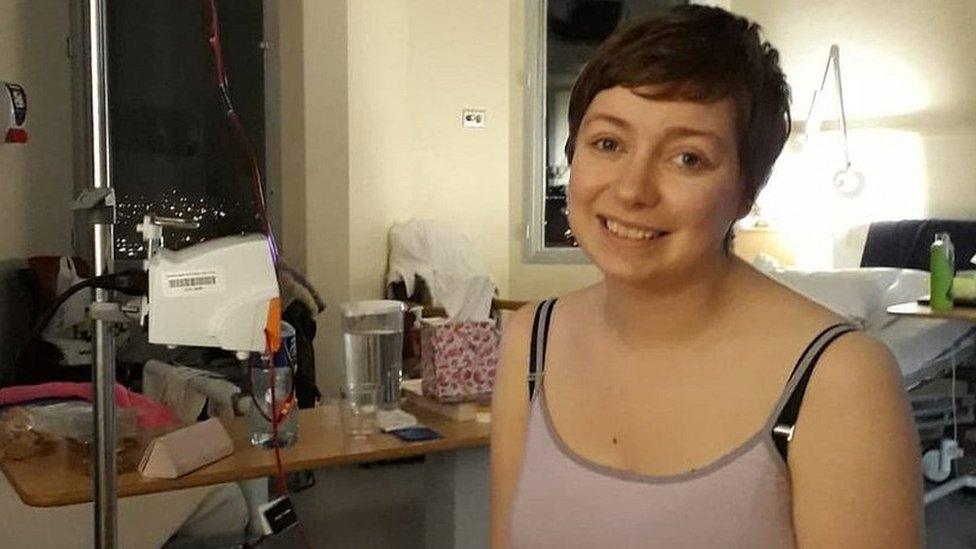 Lauren Lester in a hospital bed, sitting up an smiling at the camera