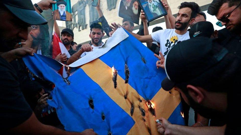 Supporters of the former paramilitary group Hashd al-Shaabi burn a Swedish flag during a protest in Baghdad's Tahrir square on July 20, 2023