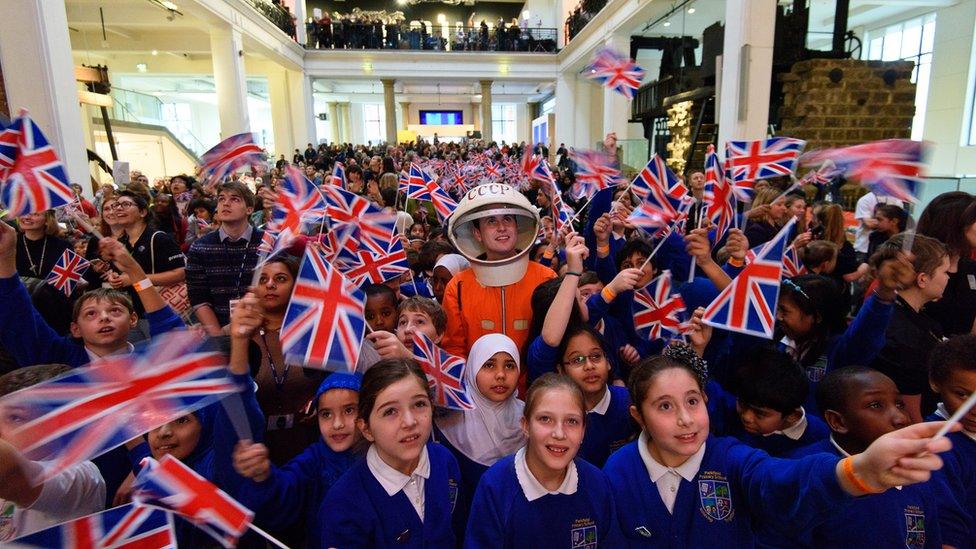 Children waving union flags, and a man standing in a mock Russian space suit at the Science Museum in London