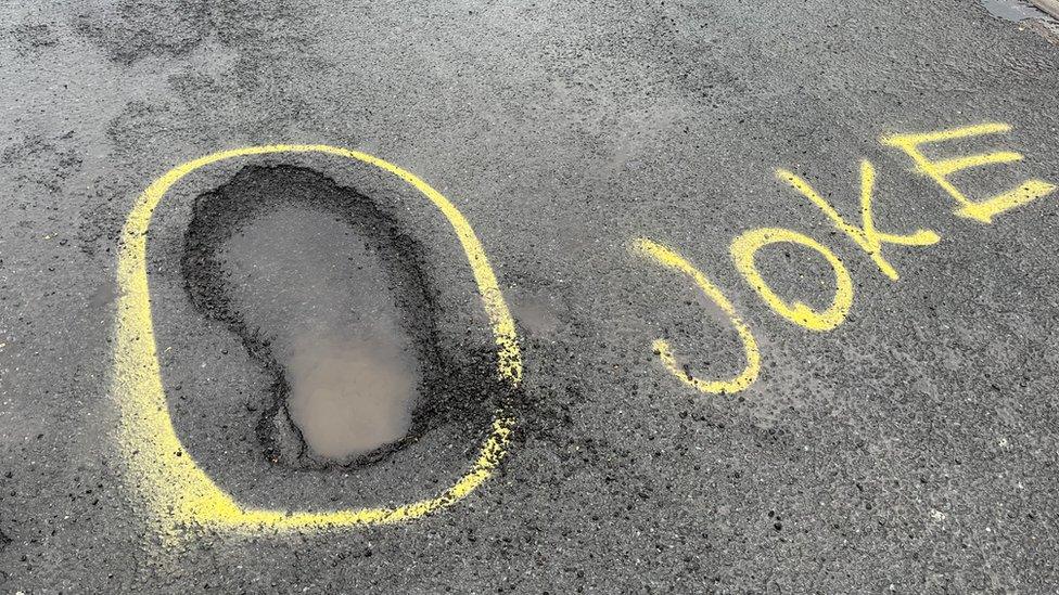 Graffiti next to pot holes on the road