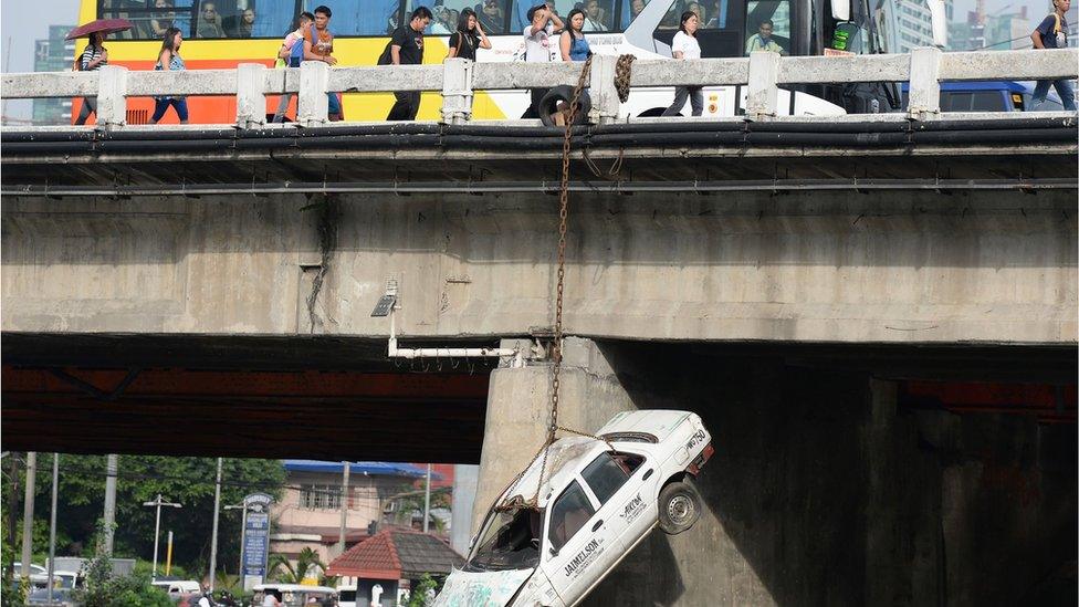 Pedestrians walk past a car suspended along a bridge in an earthquake drill as part of the metro-wide quake drill in Manila on June 22, 2016.