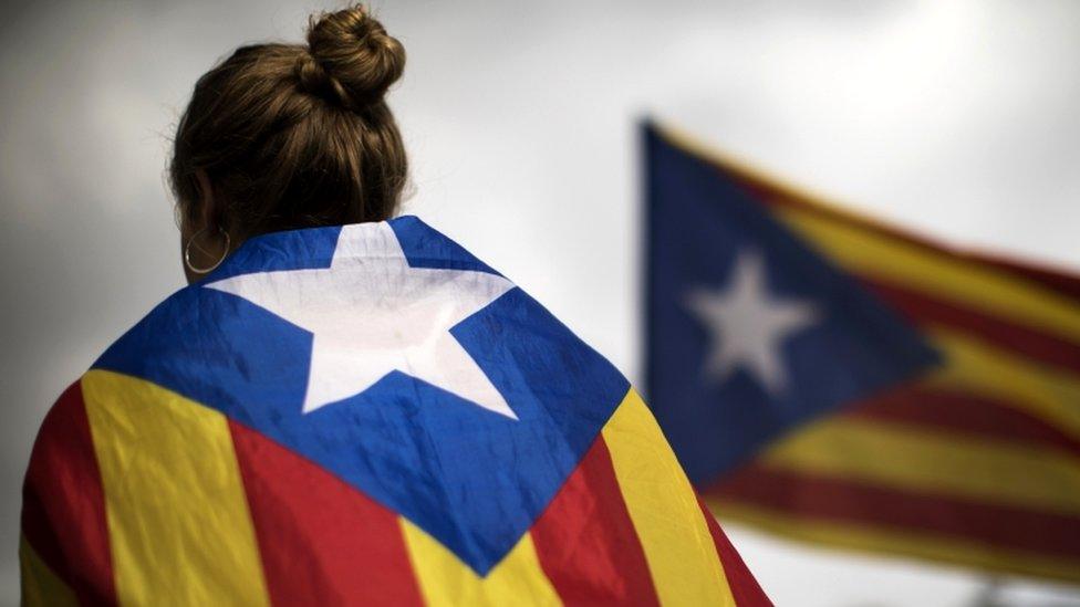 A woman has her back to the camera, draped in a Catalan flag