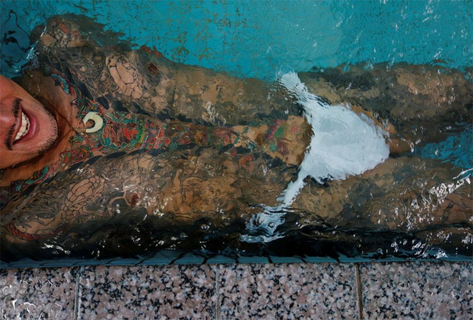 A man with body tattoos lies in a public bath