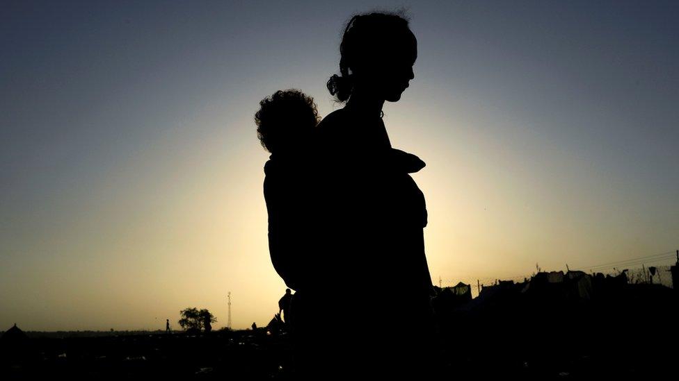 An Ethiopian woman who fled the ongoing fighting in Tigray region, carries her child near the Setit river on the Sudan-Ethiopia border