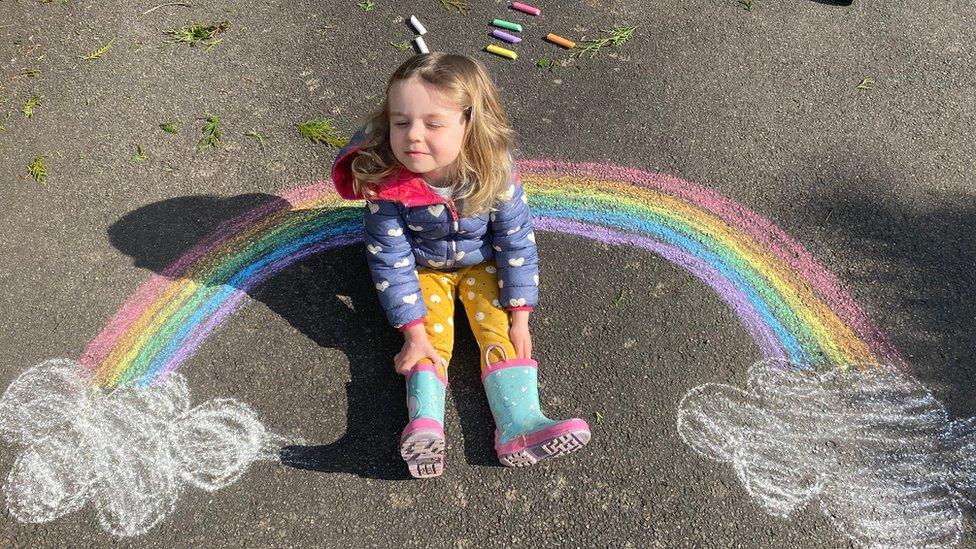 eva-sits-on-floor-next-to-chalk-rainbow-drawn-on-the-ground