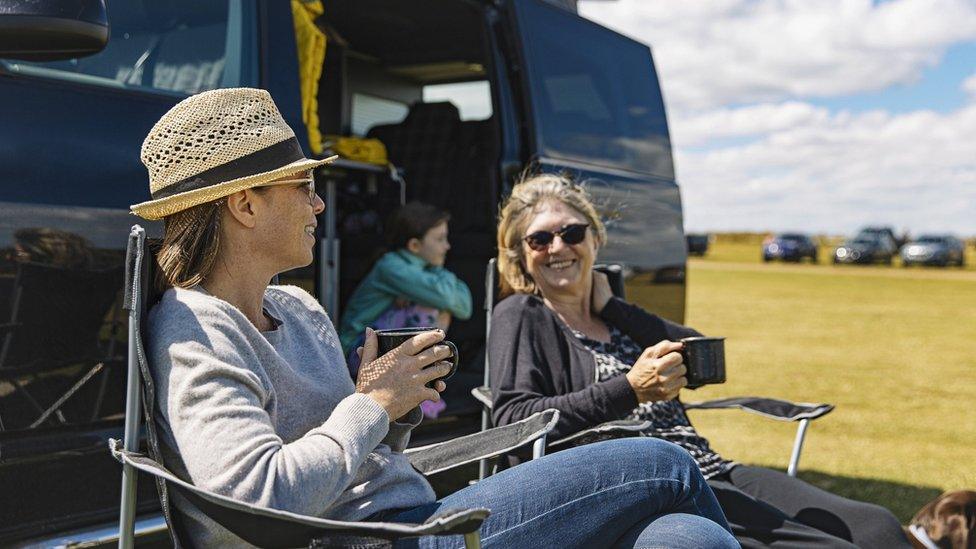 two women drinking tea by a campervan