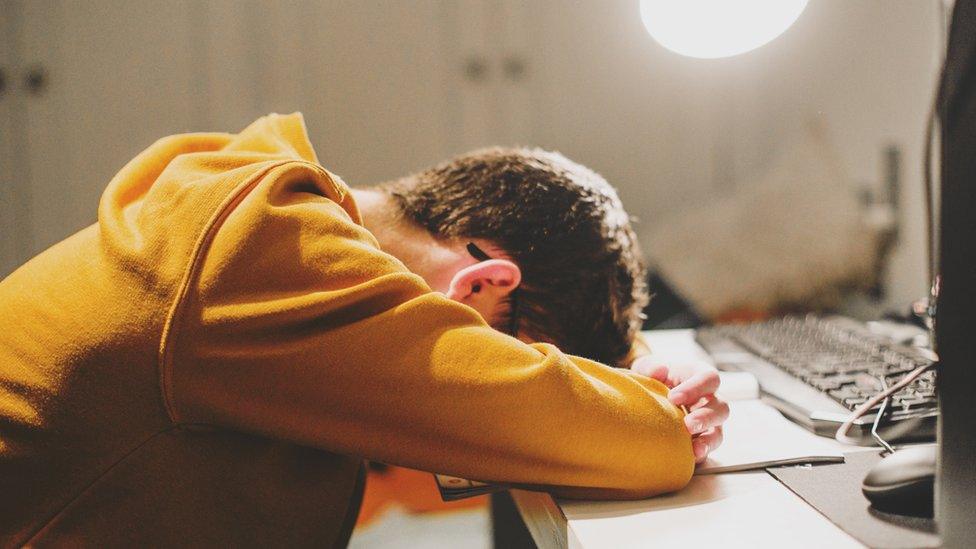 student leaning forward on his desk with arms crossed