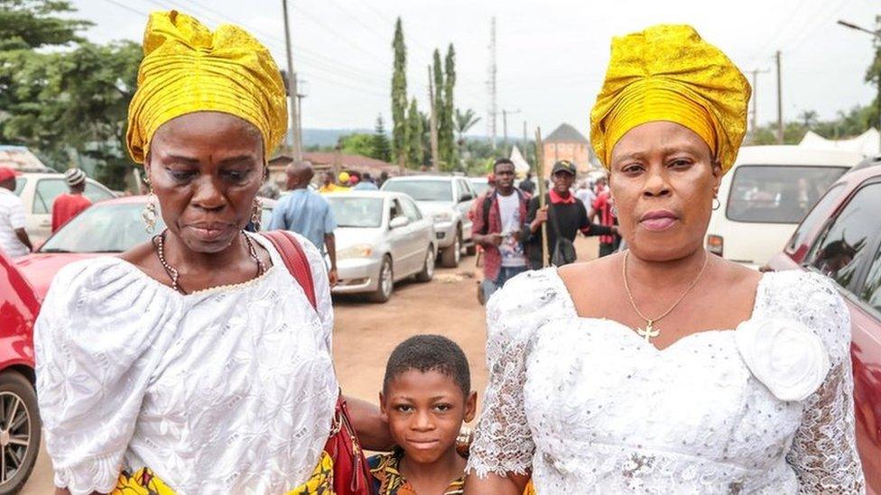 Two women in headwraps with a little boy in a street of Arondizuogu during the Ikeji Festival in Nigeria