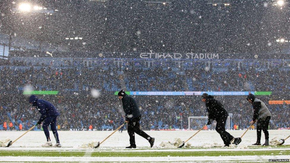 Ground staff clear the ptich of snow at half time during the Premier League match between Manchester City and West Ham United at Etihad Stadium