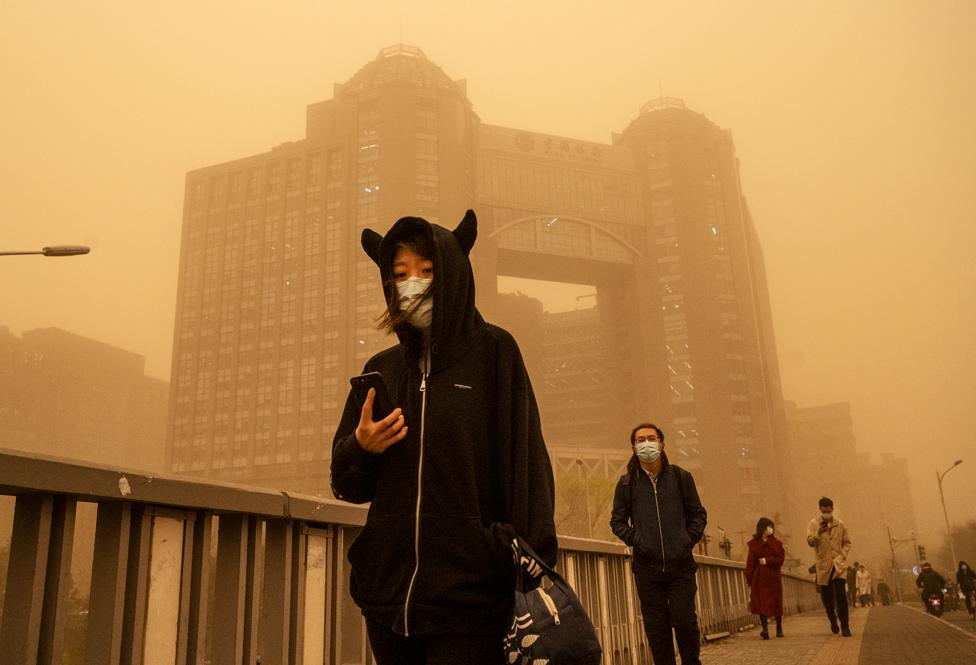 People wear protective masks as they walk along a street during a sandstorm on 15 March 2021 in Beijing, China