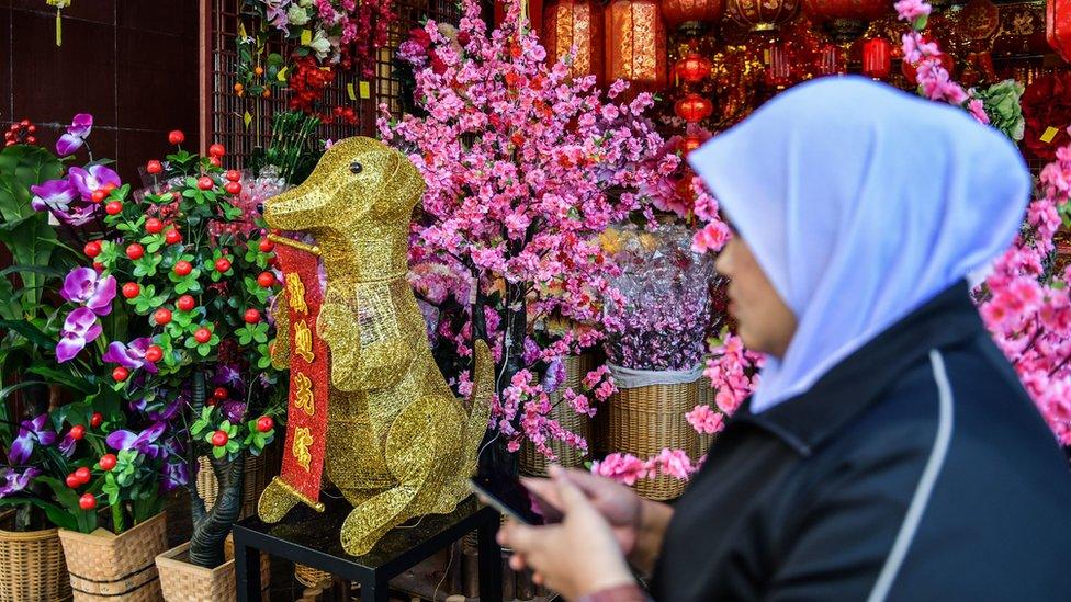 A Muslim woman walks past a golden canine statue ahead of the Lunar New Year celebrations in Kuala Lumpur's Chinatown