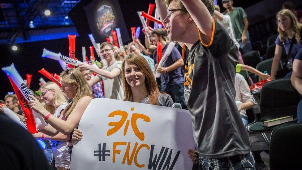 Fans hold up team banners at a League of Legends tournament