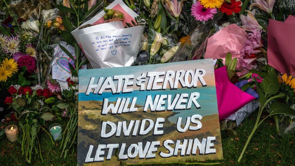 Banner reading "Hate and terror will never divide us" laid upon flowers