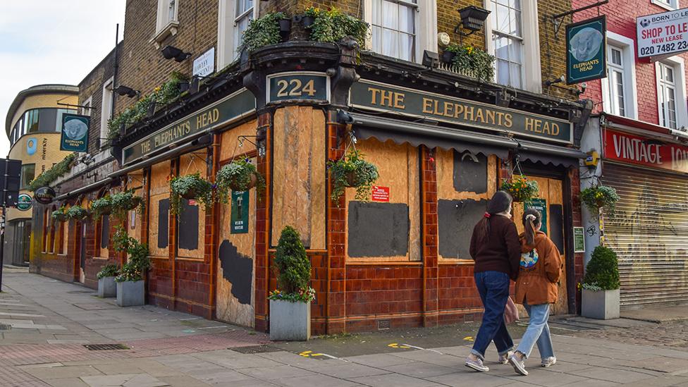 Couple walk past closed pub in Camden, London