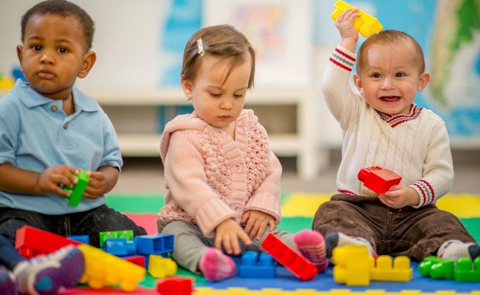 Three young children playing with plastic blocks