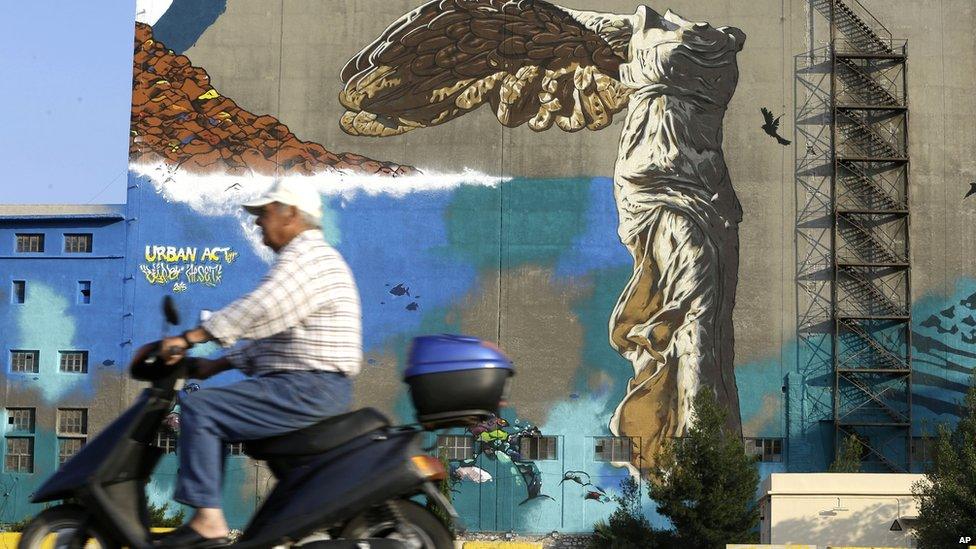 A man drives his scooter past a graffiti depicting The Winged Victory of Samothrace on the wall of an old building at the port of Piraeus, near Athens, on 28 June 2015