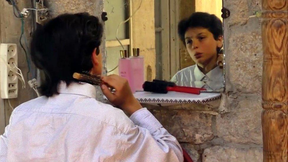 In a still from the filming of the sitcom that made him famous, Qusai Abtini brushes his hair while looking in a mirror