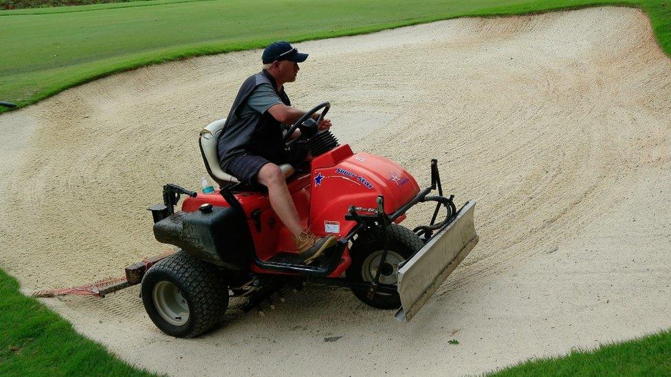 A greenkeeper attends to a bunker