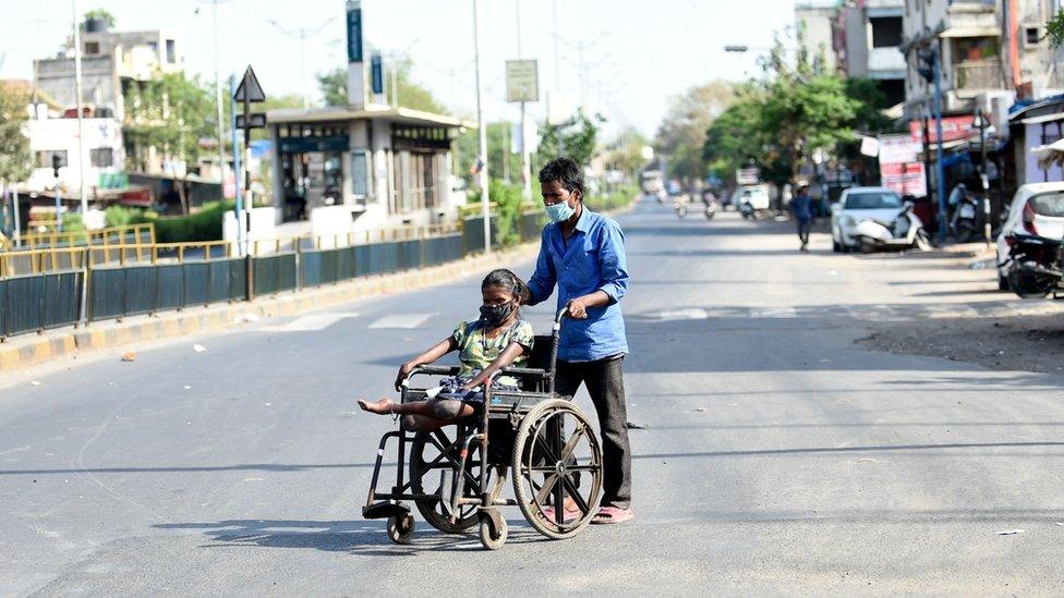 A man pushes a woman on a wheelchair as they wear facemasks during a government-imposed nationwide lockdown