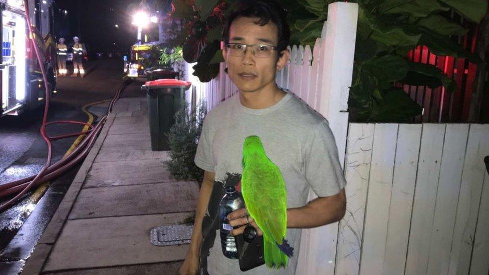 Anton Nguyen with his green parrot, Eric, stands outside his home in front of a fire truck