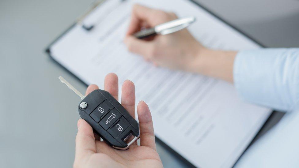 Man writing on papers on a clip chart holding car keys