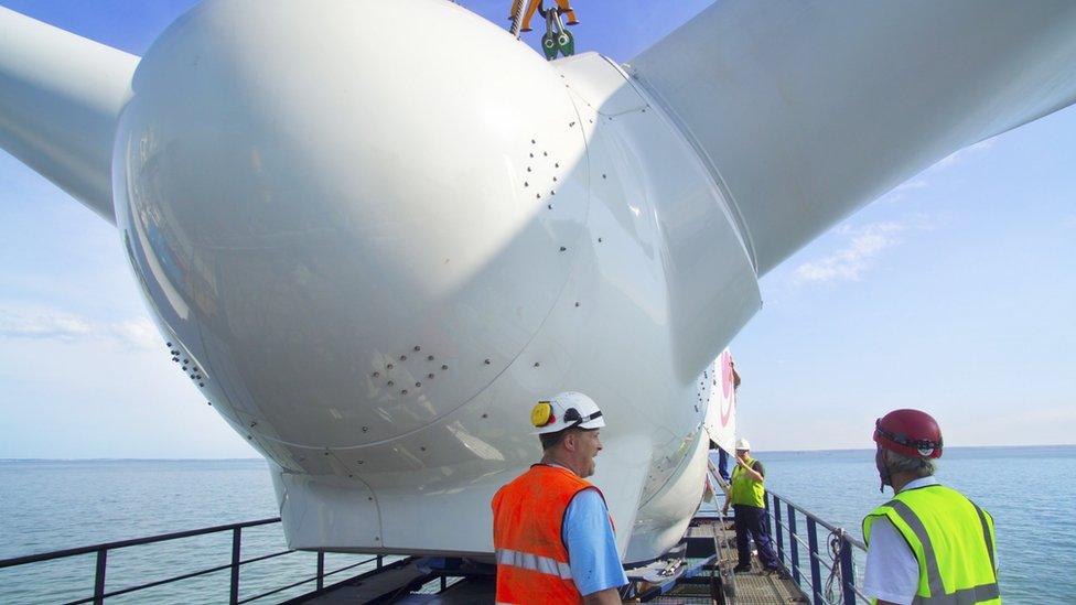 Two men stand next to wind turbine out at sea