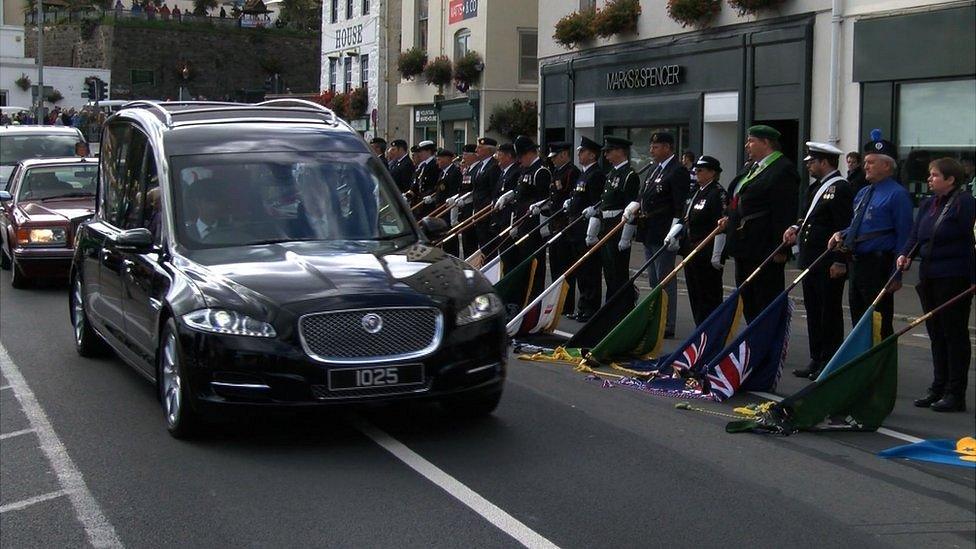 Hearse carrying Lieutenant Governor Air Marshal Peter Walker passes the guard of honour including flags of island organisations