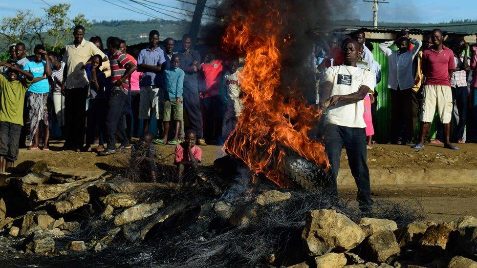 flames shooting out of a tyre as a crowd looks on