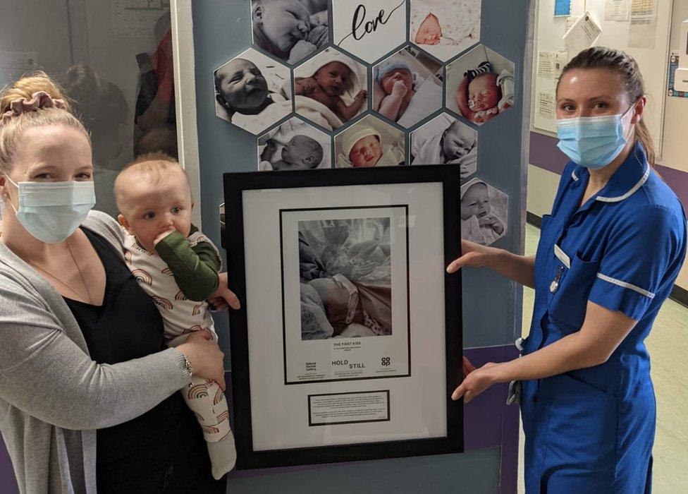 Ali Harris holding baby Indy while handing over a framed photo to a nurse