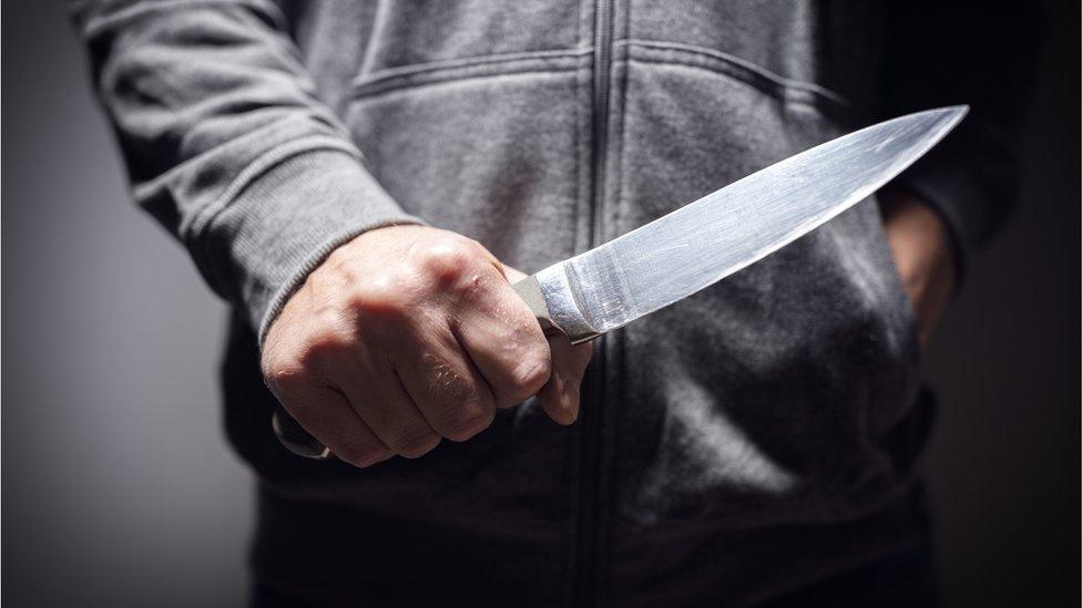 Man holding a knife in grey hoodie