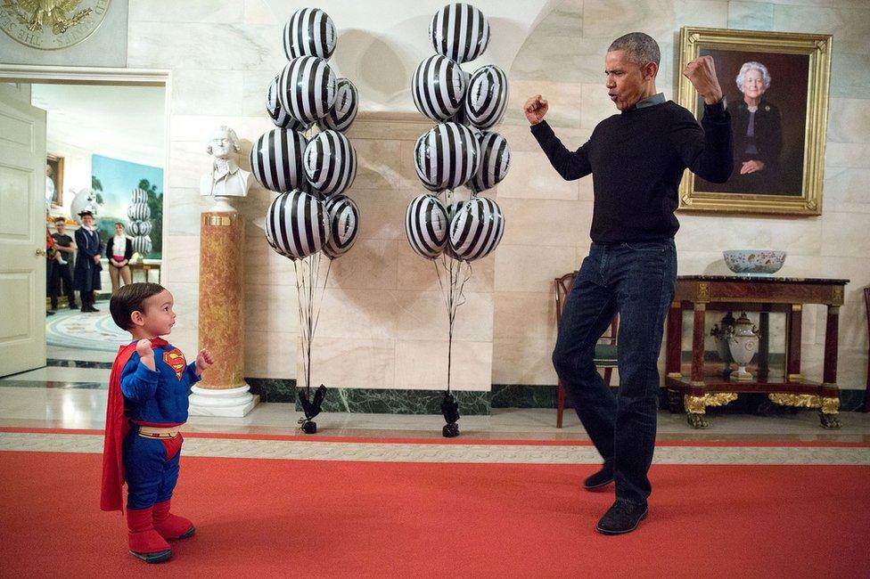 Left, a small child dressed in a superman outfit attempts to flex his muscles, while right, Mr Obama shows him how the pose is done.