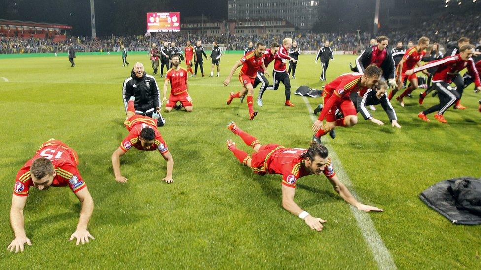 Wales team slide along the pitch in celebration