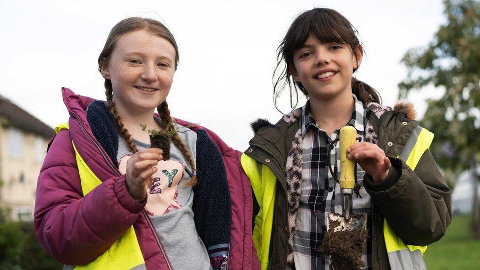 Two girls holding gardening tools and plants